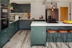 a kitchen with green cabinets and wooden stools next to an island in the middle