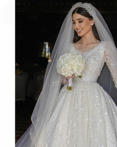 a woman in a white wedding dress holding a bouquet and smiling at the camera while wearing a veil