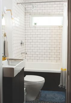 a white toilet sitting in a bathroom next to a sink and bathtub under a window