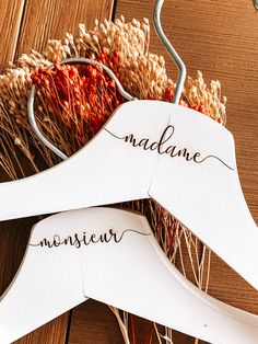 two clothes hangers with names on them sitting next to some dry grass and flowers