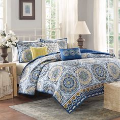 a blue and yellow comforter set with pillows on the bed in front of a window