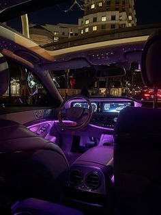 the interior of a car at night with purple lights on it and city buildings in the background