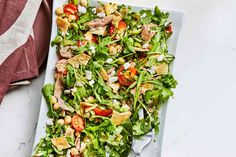 a salad with chicken, tomatoes and lettuce on a white plate next to a fork