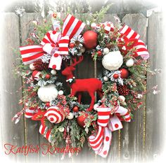 a red and white christmas wreath on a wooden fence with ornaments around the front door