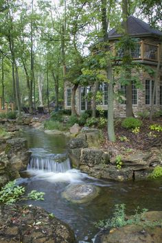 a house in the woods with a stream running through it's front yard area