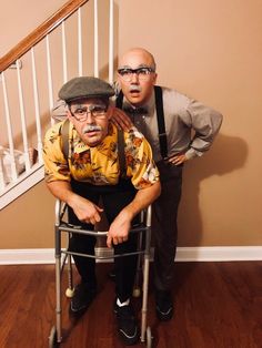 two men standing next to each other in front of a stair case with an elderly man on it