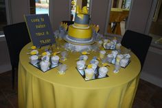 a yellow and gray wedding cake on top of a table with small cupcakes