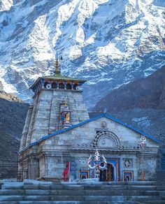 an old church in the mountains with snow covered mountains behind it and people standing outside