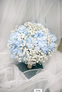 a bouquet of blue and white flowers sitting on top of a cloth covered tablecloth