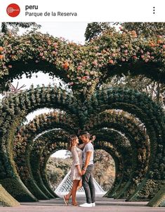 a man and woman standing in front of an archway with flowers on the sides, looking into each other's eyes