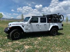 a white jeep with a bike on the back of it's bed parked in a field