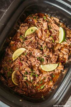 shredded pork in a slow cooker with limes and cilantro on the side