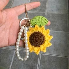 a hand holding a crocheted keychain with a sunflower on it