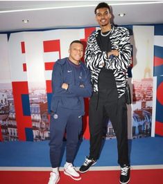 two men standing next to each other in front of a red and blue wall with letters on it