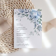 a white and blue floral wedding card on top of a woven table cloth next to a ribbon