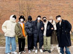 five people wearing masks standing in front of a brick wall