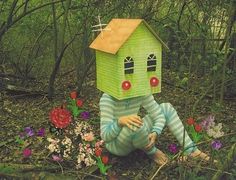 a person sitting on the ground in front of a house made out of paper and flowers