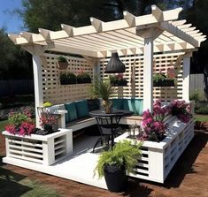 an outdoor seating area with potted plants and flowers on the table, in front of a pergolated wall