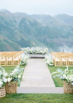 an outdoor ceremony set up with chairs and flowers on the grass in front of mountains