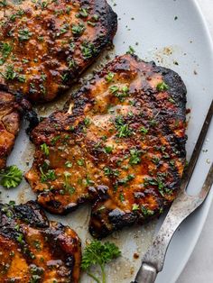 four grilled pork chops on a plate with a knife and fork next to it