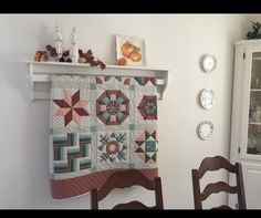 a table with a quilt hanging on the wall next to a chair and china cabinet