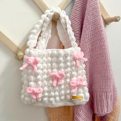 a crocheted purse hanging on the wall next to a pink sweater and scarf