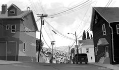 a black and white photo of a street with houses on the hill in the background