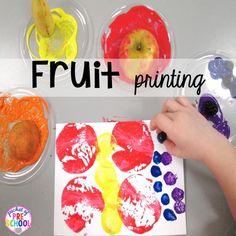 a child's hand holding a paintbrush over a paper plate with fruit paintings on it