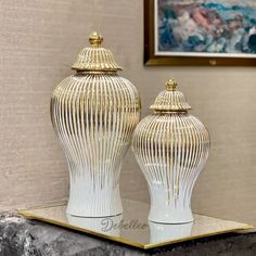 two white and gold vases sitting on top of a marble shelf next to a painting