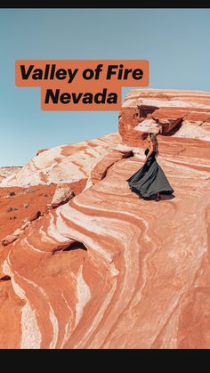 a woman in a long black dress standing on top of a red rock formation with her arms outstretched