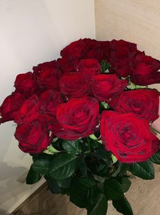 a bouquet of red roses sitting on top of a table next to a wall with a hand holding it