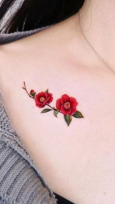 a woman's chest with two red flowers on the left side of her neck