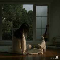 a woman sitting on the floor next to a white dog and looking at an open book