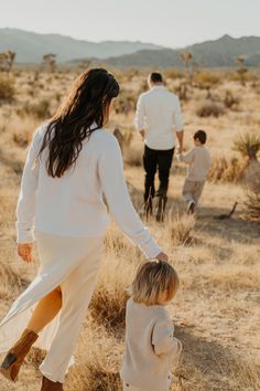 a woman holding the hand of a small child as they walk through an open field