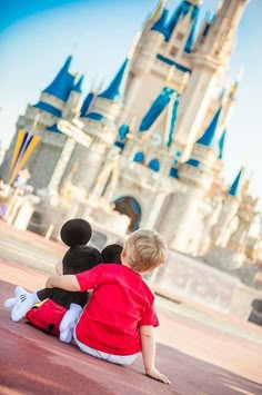 two children sitting on the ground in front of a castle with mickey and minnie mouse