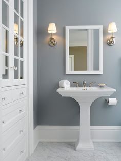 a white pedestal sink sitting under a mirror next to a bathroom vanity with two lights on it