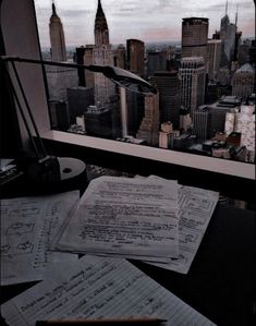 some papers are sitting on top of a desk in front of a window with a view of the city