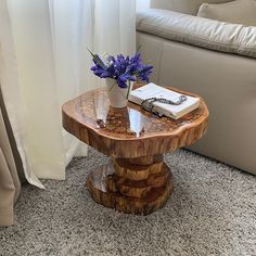 a table with a book and flowers on it sitting in front of a couch next to a window