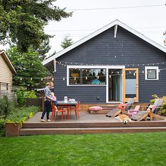 a woman standing on top of a wooden deck in front of a blue house with lawn chairs