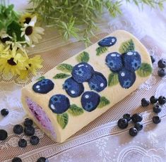 a roll with blueberries painted on it next to some flowers and berries in the background