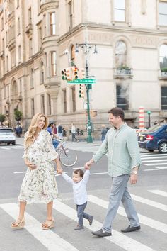 a man and woman holding hands while walking across a crosswalk with a small child