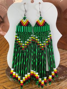 a pair of green, yellow and red beaded earrings on top of a wooden table