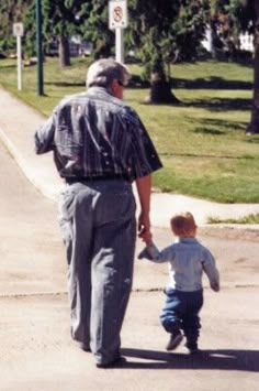 an older man holding the hand of a young boy as they walk down a sidewalk