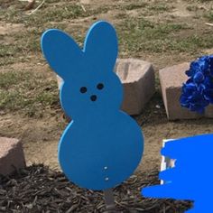 a blue bunny shaped yard stake next to some flowers and bricks on the ground in front of it