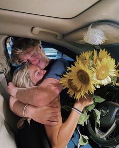 a man and woman hugging in the back seat of a car with sunflowers