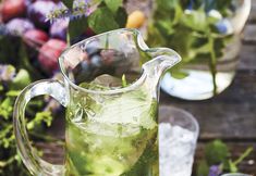 a pitcher filled with green liquid sitting on top of a table next to glasses and flowers