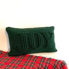 a green knitted pillow sitting on top of a plaid blanket