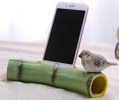 a small bird sitting on top of a green pipe next to a cell phone holder