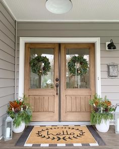 the front door is decorated with wreaths and two potted plants on either side