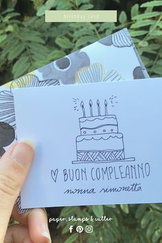 someone holding up two birthday cards in front of some trees and bushes with the words v buon compleanoo on them